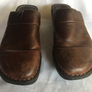 May include: A pair of brown leather slip-on clogs with a black rubber sole.