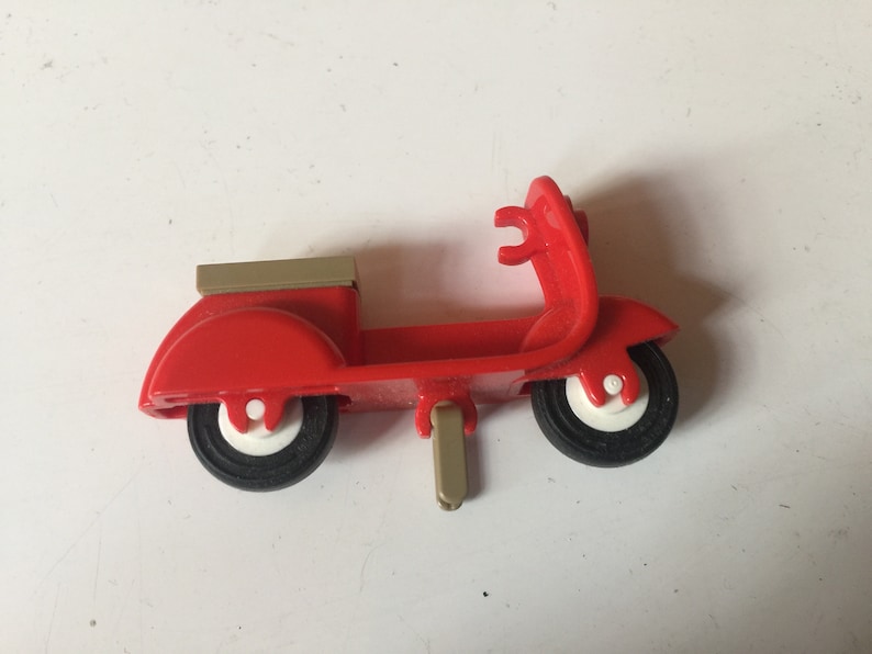 May include: A red toy scooter with a gold-colored seat and a white kickstand. The scooter has black wheels with white centers.
