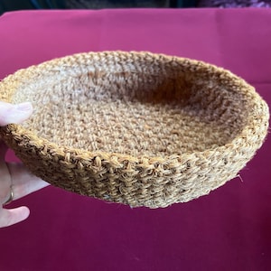 May include: A round, woven basket made of natural fibers. The basket is light brown and has a smooth, textured surface.