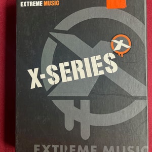 Może przedstawiać: Czarna kaseta DVD z czerwono-białym logo z napisem "X-Series" oraz tekstem "The Entire X-Series on Two DVDs" i "Extreme Music".