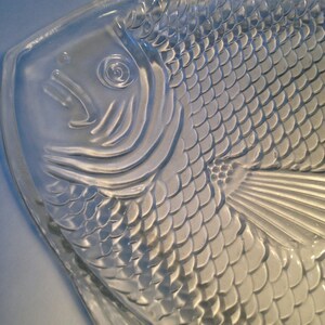 May include: A clear glass serving dish shaped like a fish with a detailed design of scales and fins.