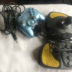 Op de afbeelding: Een blauwe en zwarte videogamecontroller met een zwart snoer en een zwarte en gele videogamejoystick met een zwart snoer.