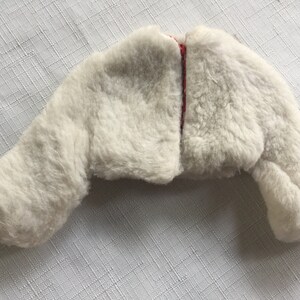 May include: A white faux fur jacket with a red and black plaid lining. The jacket has long sleeves and a cropped length.