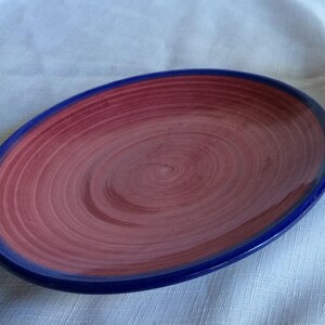 May include: A red and blue ceramic plate with a swirl design. The plate has a blue rim and a red center with a swirl pattern.