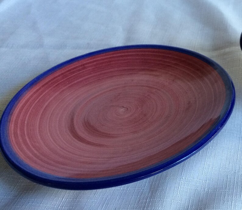 May include: A red and blue ceramic plate with a swirl design. The plate has a blue rim and a red center with a swirl pattern.