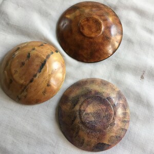 May include: Three wooden bowls with different patterns and colors. The bowls are brown, tan, and purple with a speckled pattern.
