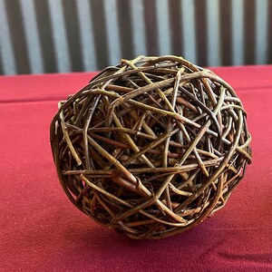 May include: A brown woven sphere made of thin twigs, sitting on a red surface.