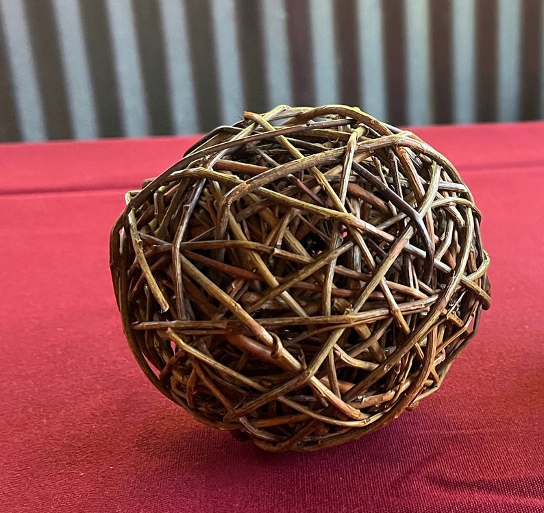 May include: A brown woven sphere made of thin twigs, sitting on a red surface.