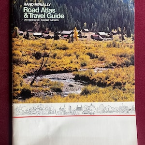 以下が含まれることがあります： ヴィンテージのRand McNally Road Atlas & Travel Guide。表紙には、川、木、建物のある風景が描かれています。タイトルは白い文字です。表紙の下部には、白枠に白黒のイラストが描かれています。