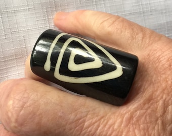 May include: Black ceramic ring with a white geometric design. The ring is wide and has a cylindrical shape.