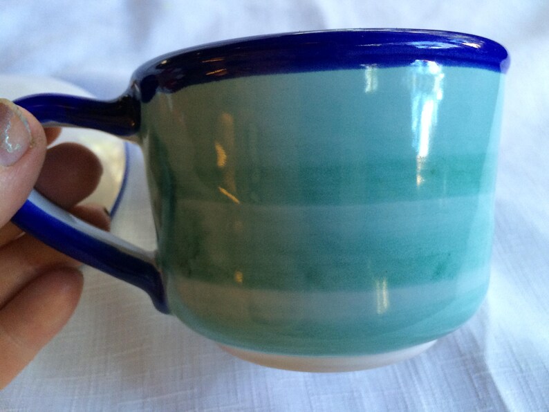 May include: A blue and green striped ceramic teacup with a blue rim.