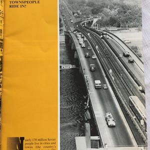 May include: A black and white photo of a bridge over a river with cars driving on it. The text "Along the Dnieper and over it. One of the new bridges in Kiev, capital of the Ukrainian SSR" is at the bottom of the image.