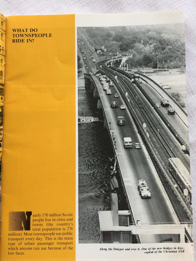 May include: A black and white photo of a bridge over a river with cars driving on it. The text "Along the Dnieper and over it. One of the new bridges in Kiev, capital of the Ukrainian SSR" is at the bottom of the image.