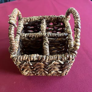 May include: Woven basket with four compartments and two arched handles. The basket is made of natural-colored, tightly woven fibers. The basket is designed to hold items and is suitable for home decor.