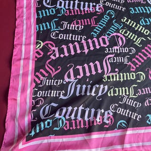 Puede incluir: Una bufanda de seda negra con un borde rosa. La bufanda está cubierta con un patrón repetido de las palabras "Juicy Couture" en varios colores, incluyendo rosa, azul y verde.