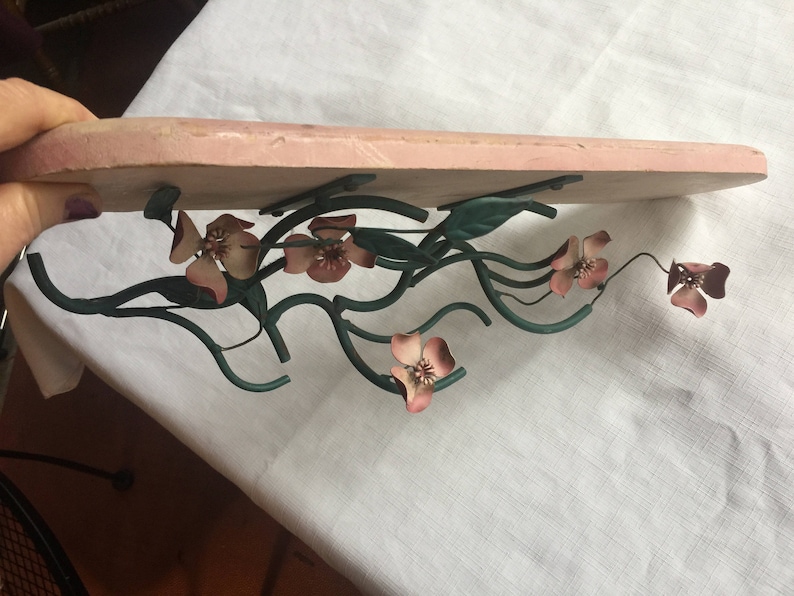 May include: A pink shelf bracket with a metal floral design. The design features pink flowers and green leaves.