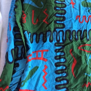 K&ouml;nnte beinhalten: Ein blauer, gr&uuml;ner und roter Stoff mit einem sich wiederholenden Muster aus abstrakten Formen und Linien. Der Stoff hat eine strukturierte Oberfl&auml;che und ein leicht verblichenes Aussehen.