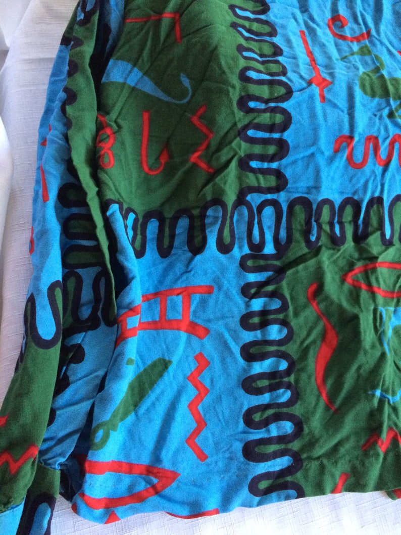 K&ouml;nnte beinhalten: Ein blauer, gr&uuml;ner und roter Stoff mit einem sich wiederholenden Muster aus abstrakten Formen und Linien. Der Stoff hat eine strukturierte Oberfl&auml;che und ein leicht verblichenes Aussehen.