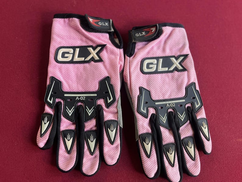 Puede incluir: Par de guantes de moto GLX rosas. Los guantes tienen detalles en negro y el logotipo GLX en blanco. Los guantes tienen una textura de malla y el texto "A-02" es visible.