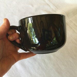 May include: A large, black ceramic mug with a wide, rounded bowl and a handle. The mug is glossy and reflects light.