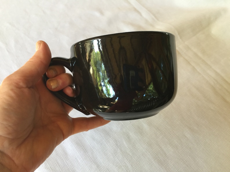May include: A large, black ceramic mug with a wide, rounded bowl and a handle. The mug is glossy and reflects light.
