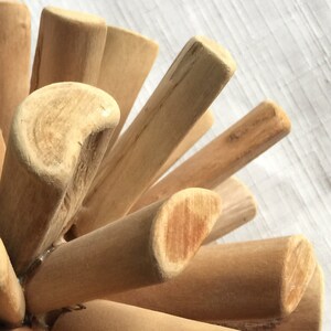 May include: A close-up of a wooden sculpture made of many small sticks, all joined together in a circular shape. The sticks are all natural wood color and have a smooth finish.