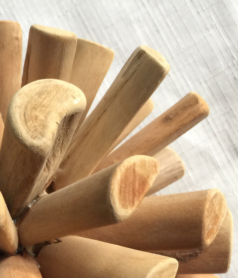 May include: A close-up of a wooden sculpture made of many small sticks, all joined together in a circular shape. The sticks are all natural wood color and have a smooth finish.