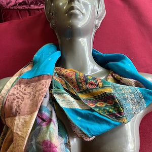 May include: A colorful patchwork scarf made of different fabrics in shades of blue, pink, green, and brown. The scarf is draped around a mannequin's neck.