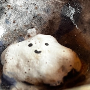 May include: A white ceramic bowl with a dark brown glaze and a white cloud-shaped object with a black smiley face inside.