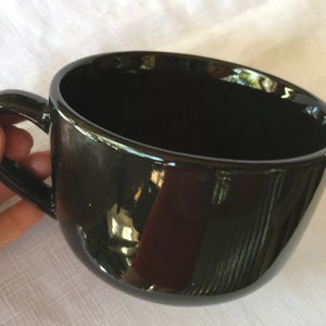 May include: A large, black ceramic mug with a wide, rounded bowl and a handle. The mug is glossy and reflects light.