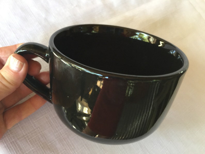May include: A large, black ceramic mug with a wide, rounded bowl and a handle. The mug is glossy and reflects light.
