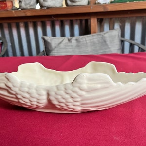 May include: A white ceramic bowl shaped like a seashell with a textured surface. The bowl is on a red surface.