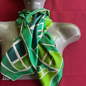 May include: A green silk scarf with a geometric pattern of squares and rectangles. The scarf is tied around a mannequin's neck.