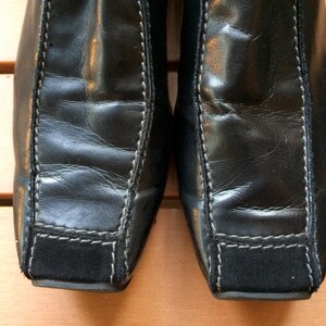 Puede incluir: Un par de botines de cuero negro con punta cuadrada y un panel de gamuza en el tal&oacute;n.