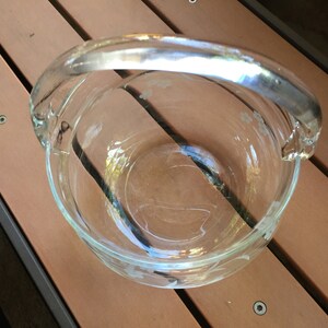 May include: A clear glass bowl with a handle. The bowl has a floral design etched into the glass.
