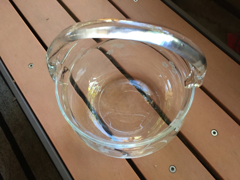 May include: A clear glass bowl with a handle. The bowl has a floral design etched into the glass.