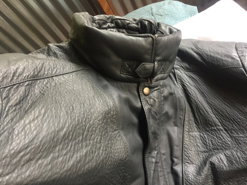 Pu&ograve; includere: Una giacca di pelle nera con colletto alto e chiusura con bottone. La giacca ha una superficie testurizzata e un design semplice.