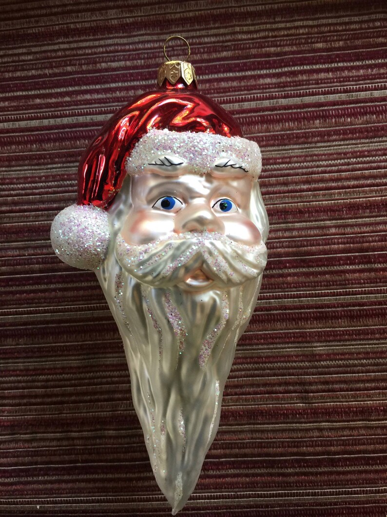 以下が含まれることがあります： サンタクロースの形をしたヴィンテージのクリスマスオーナメント。オーナメントは、白いグリッタートリムが付いた赤い帽子、青い目、長い銀色のひげが特徴です。吊り下げ用の金色の金属ループが付いています。