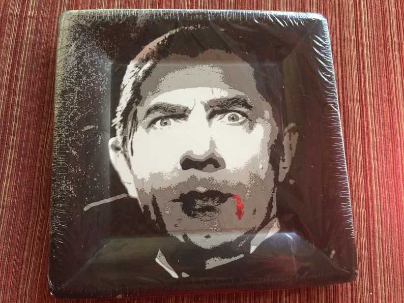 May include: A black and white paper plate with a graphic of a man's face with a red drip of blood on his chin. The man has a surprised expression on his face.