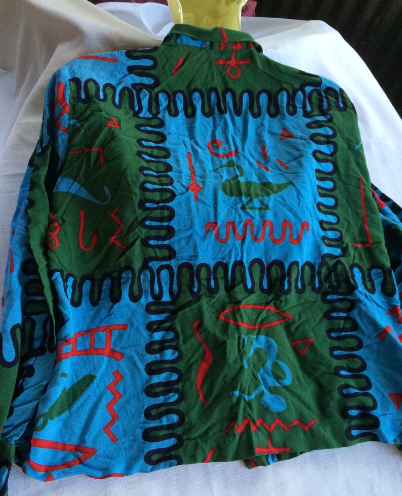 K&ouml;nnte beinhalten: Ein lang&auml;rmliges Hemd mit einem farbenfrohen abstrakten Muster in Blaut&ouml;nen, Gr&uuml;n, Rot und Schwarz. Das Muster zeigt geometrische Formen und Linien.