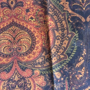May include: Close-up of a fabric with a detailed paisley pattern. The design features a mix of warm colors, including shades of orange, red, and brown, contrasted with deep navy blue. The intricate pattern is reminiscent of traditional textile designs.
