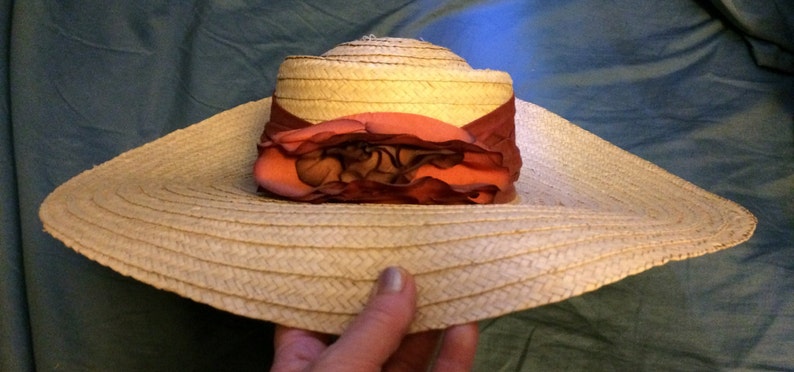 Pu&ograve; includere: Un cappello di paglia a tesa larga con un accento di fiore rosa e bordeaux.