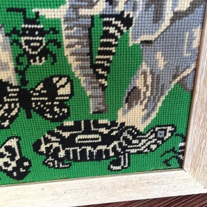 May include: A framed needlepoint piece with a green background and a variety of colorful embroidered designs, including butterflies, insects, and a turtle.