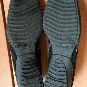 Puede incluir: Un par de zapatos de ante negro con suela de goma texturizada. Los zapatos tienen el nombre de la marca "Paul Green" impreso en la suela. La talla es 7 1/2.