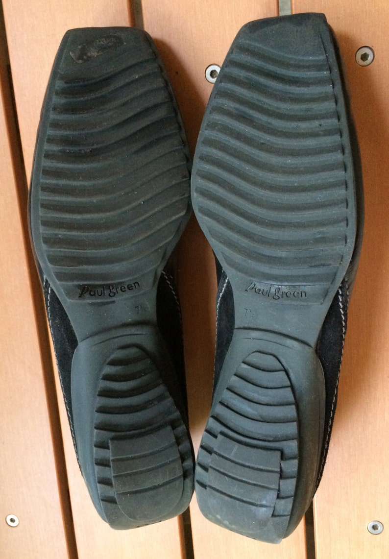 Puede incluir: Un par de zapatos de ante negro con suela de goma texturizada. Los zapatos tienen el nombre de la marca "Paul Green" impreso en la suela. La talla es 7 1/2.