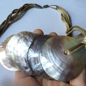 May include: A multi-strand suede necklace with a large, layered pendant made of iridescent mother-of-pearl shells.