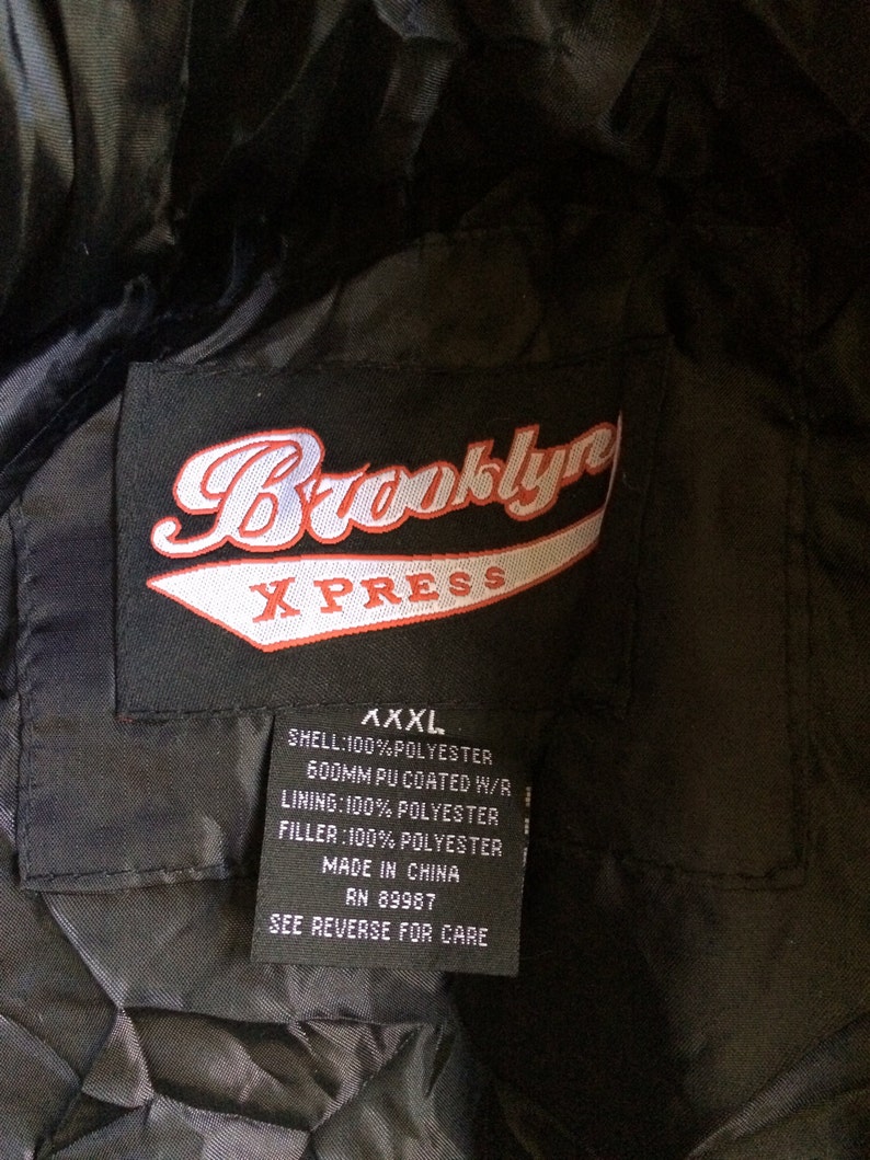 Puede incluir: Una chaqueta negra con un parche de logotipo Brooklyn XPRESS rojo y blanco. La etiqueta indica que la chaqueta es XXXL, hecha de 100% poli&eacute;ster y fabricada en China. La etiqueta tambi&eacute;n incluye instrucciones de cuidado.