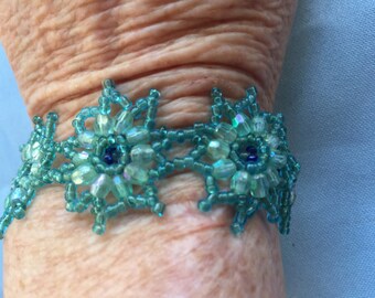 May include: A turquoise beaded bracelet with a floral design. The bracelet is made with small, iridescent beads and features blue accents.