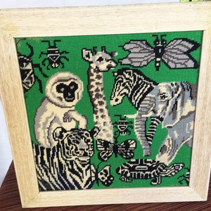 May include: A framed needlepoint picture with a green background featuring a variety of animals including a zebra, giraffe, elephant, monkey, tiger, and butterflies.