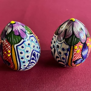 May include: Two ceramic salt and pepper shakers shaped like eggs. The shakers are decorated with colorful floral patterns and yellow dots.